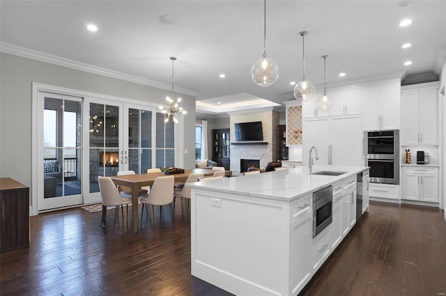 kitchen with white cabinets, sink, a center island with sink, and a fireplace