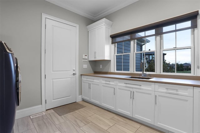 kitchen featuring white cabinets, stainless steel fridge, crown molding, and sink