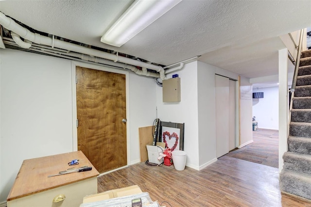 basement with a textured ceiling, hardwood / wood-style flooring, and electric panel