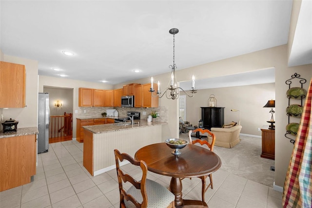 kitchen featuring kitchen peninsula, appliances with stainless steel finishes, hanging light fixtures, a chandelier, and light stone counters