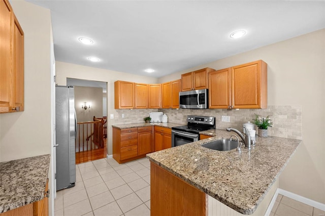 kitchen featuring appliances with stainless steel finishes, sink, kitchen peninsula, light stone counters, and light tile patterned floors