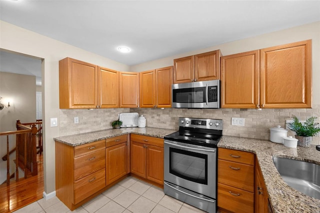 kitchen featuring light tile patterned floors, appliances with stainless steel finishes, light stone counters, and tasteful backsplash