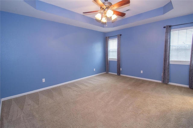 carpeted spare room with ceiling fan and a raised ceiling