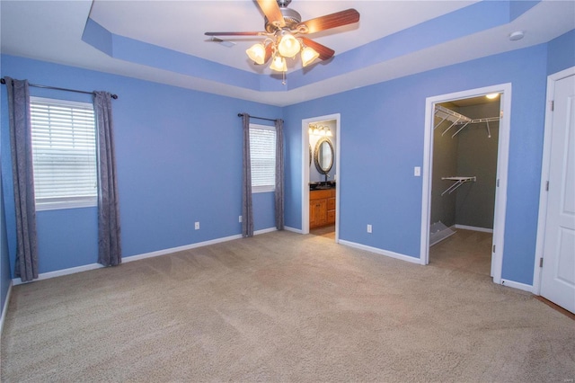 unfurnished bedroom featuring multiple windows, light carpet, and a tray ceiling