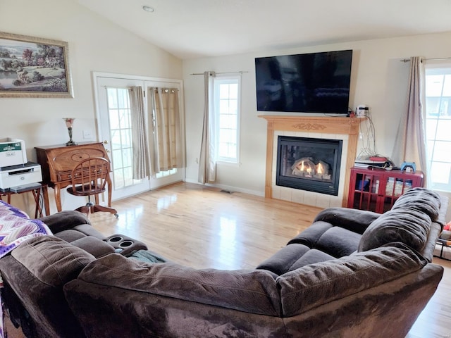 living room featuring a fireplace, lofted ceiling, light wood-type flooring, and a healthy amount of sunlight