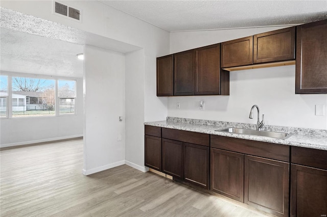 kitchen with a textured ceiling, dark brown cabinets, light stone counters, and sink