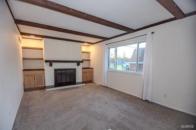 unfurnished living room with a brick fireplace, beam ceiling, and carpet flooring