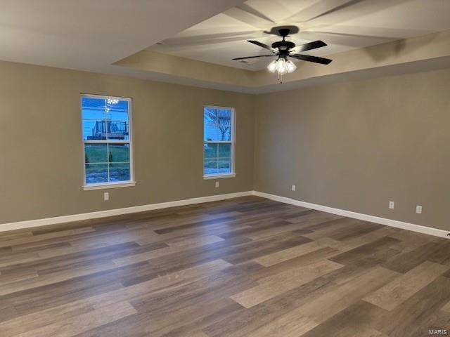 empty room with a raised ceiling, ceiling fan, and dark wood-type flooring