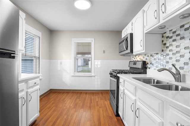 kitchen with sink, stainless steel appliances, hardwood / wood-style floors, white cabinets, and tile walls