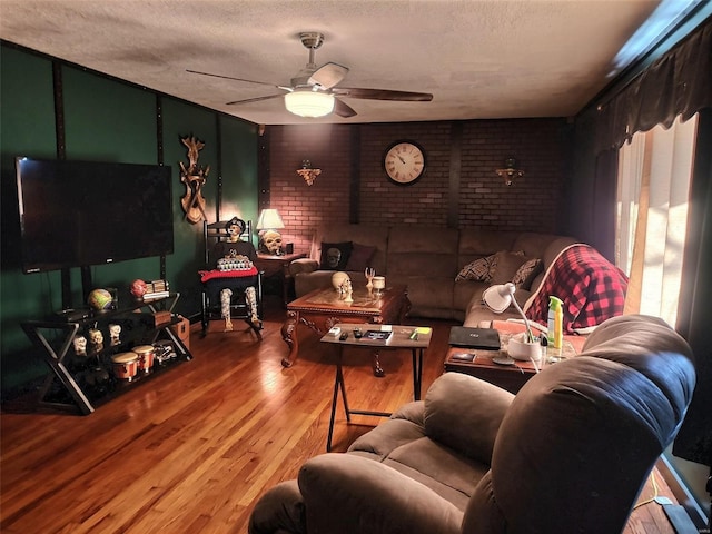 living room with ceiling fan, wood-type flooring, a textured ceiling, and brick wall