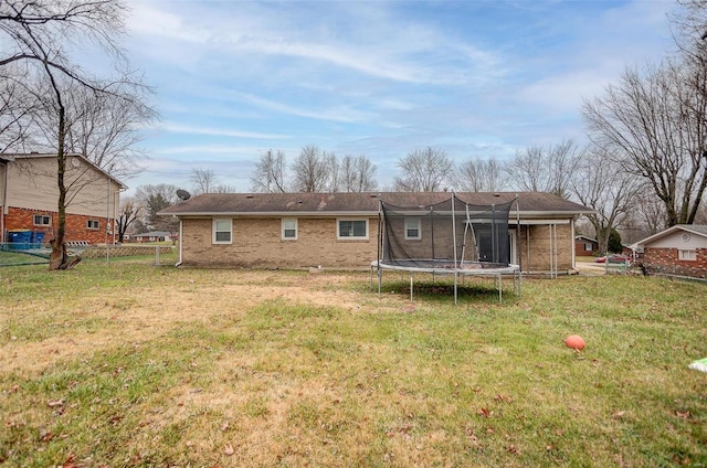 back of property with a trampoline and a yard