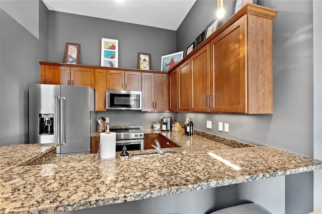 kitchen featuring sink, light stone counters, kitchen peninsula, a kitchen bar, and appliances with stainless steel finishes