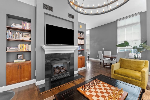 living room with built in shelves, dark hardwood / wood-style floors, and a chandelier