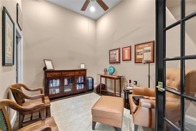 sitting room featuring ceiling fan, carpet floors, and a towering ceiling