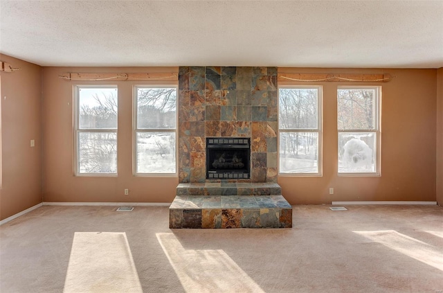 unfurnished living room with a stone fireplace, carpet floors, and a textured ceiling