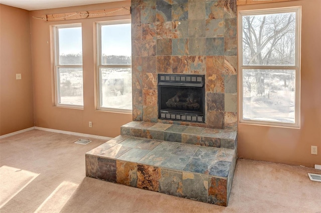 living room with a tile fireplace, light carpet, and plenty of natural light