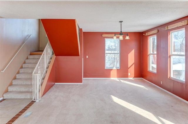 interior space with a notable chandelier, light colored carpet, a textured ceiling, and a wealth of natural light