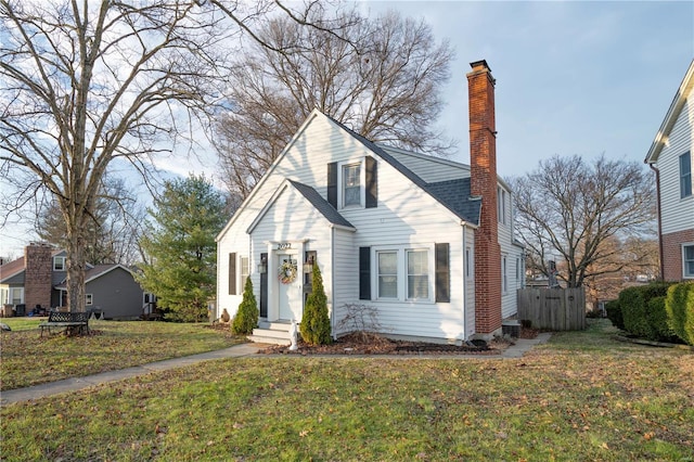 view of front facade with a shingled roof, fence, a chimney, and a front lawn