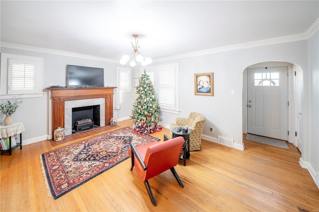 living room with crown molding, plenty of natural light, a premium fireplace, and an inviting chandelier