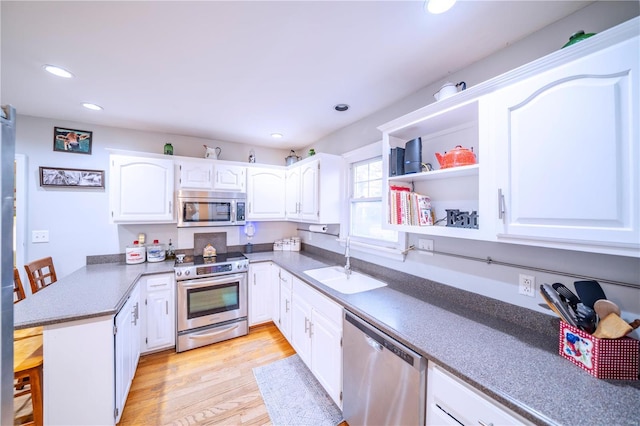 kitchen featuring white cabinetry, sink, light hardwood / wood-style flooring, kitchen peninsula, and appliances with stainless steel finishes