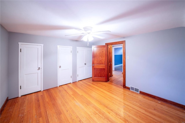 unfurnished bedroom featuring ceiling fan, light hardwood / wood-style floors, and two closets