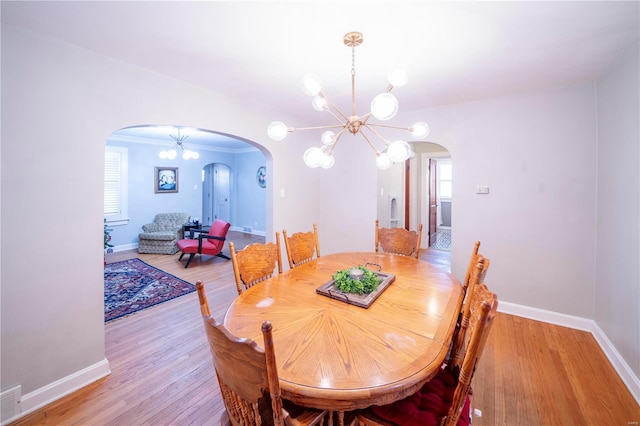 dining room with light wood-type flooring, baseboards, a chandelier, and arched walkways