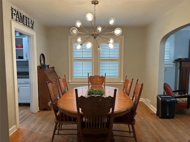 dining area with arched walkways, an inviting chandelier, baseboards, and wood finished floors