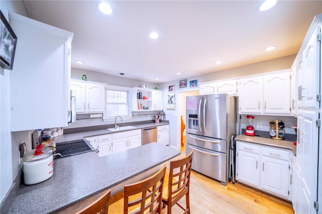 kitchen featuring recessed lighting, stainless steel appliances, a peninsula, a sink, and light wood-type flooring