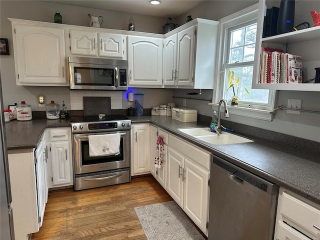 kitchen with stainless steel appliances, wood finished floors, a sink, white cabinetry, and dark countertops