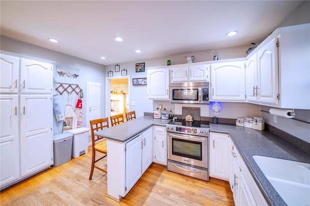 kitchen with stainless steel appliances, a peninsula, a sink, and light wood-style floors