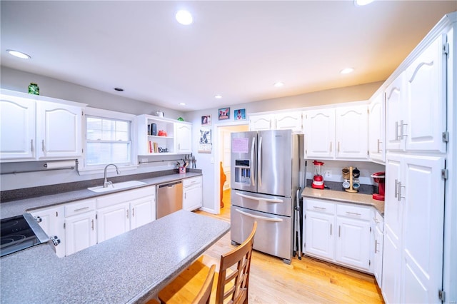 kitchen with a peninsula, a sink, white cabinets, light wood-style floors, and appliances with stainless steel finishes