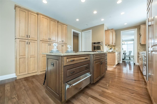 kitchen featuring light stone counters, wood finished floors, stainless steel oven, a center island, and a warming drawer