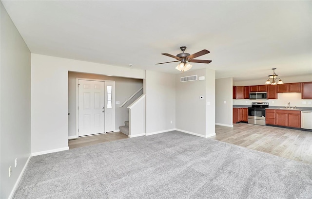 unfurnished living room with sink, light colored carpet, and ceiling fan with notable chandelier