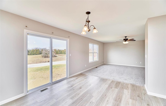 unfurnished room with ceiling fan with notable chandelier and light hardwood / wood-style flooring