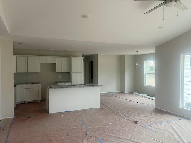 kitchen featuring pendant lighting, a center island, stone counters, white cabinets, and ceiling fan with notable chandelier