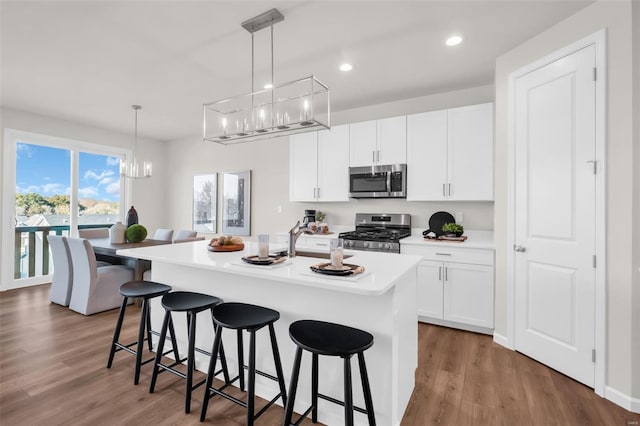 kitchen featuring white cabinets, decorative light fixtures, stainless steel appliances, and an island with sink