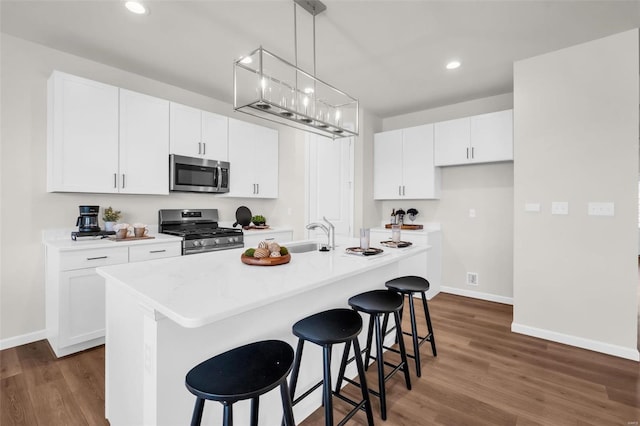 kitchen featuring pendant lighting, a breakfast bar, an island with sink, appliances with stainless steel finishes, and white cabinetry