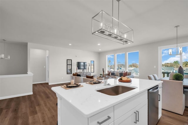 kitchen featuring dark wood-type flooring, sink, decorative light fixtures, a center island with sink, and white cabinets