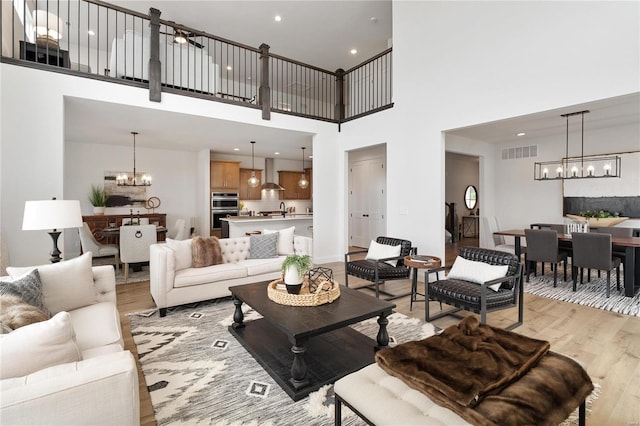 living room with light hardwood / wood-style flooring, a towering ceiling, a chandelier, and sink