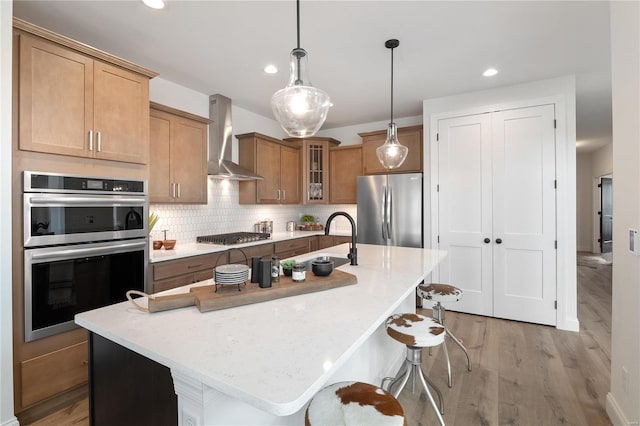 kitchen with a breakfast bar, stainless steel appliances, a kitchen island with sink, and wall chimney exhaust hood