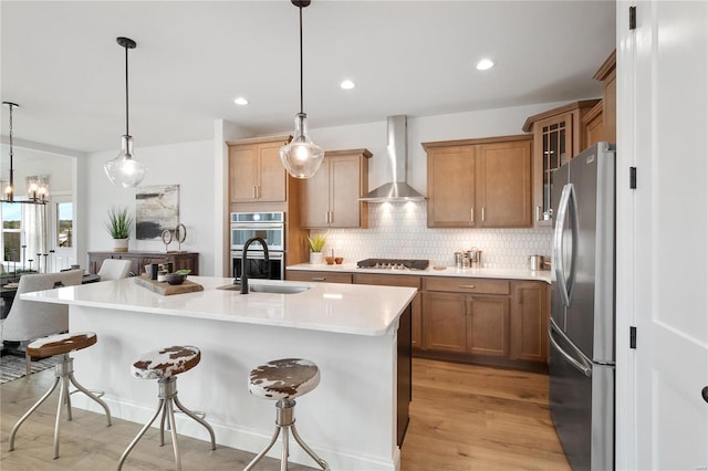 kitchen with pendant lighting, a kitchen island with sink, wall chimney exhaust hood, a kitchen bar, and stainless steel appliances