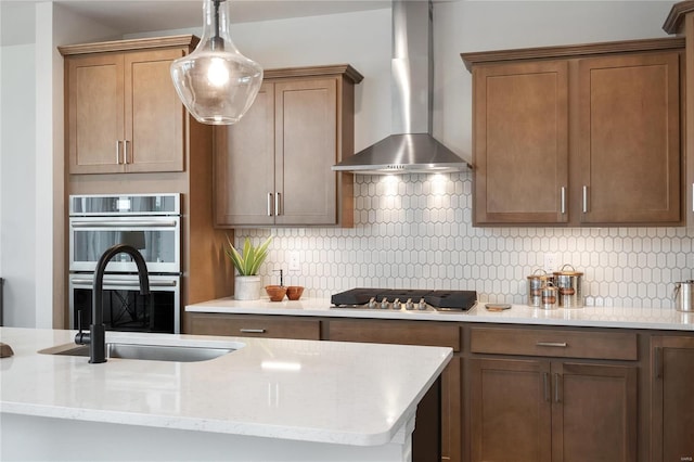 kitchen with backsplash, sink, wall chimney exhaust hood, light stone countertops, and stainless steel appliances