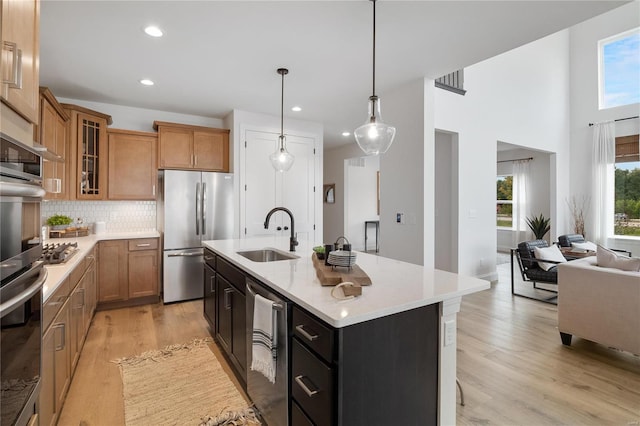 kitchen with sink, backsplash, pendant lighting, a kitchen island with sink, and appliances with stainless steel finishes