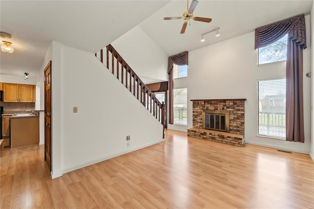 living room featuring a brick fireplace, plenty of natural light, ceiling fan, and light wood-type flooring