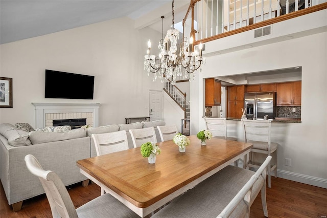 dining area with a notable chandelier, dark wood-type flooring, a fireplace, high vaulted ceiling, and beamed ceiling