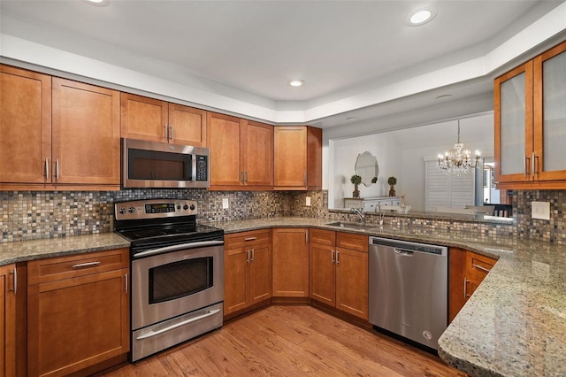 kitchen featuring light stone countertops, appliances with stainless steel finishes, an inviting chandelier, decorative backsplash, and sink