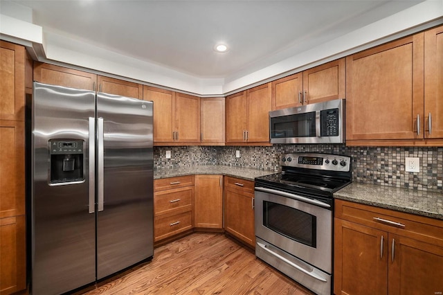 kitchen featuring light hardwood / wood-style floors, decorative backsplash, appliances with stainless steel finishes, and dark stone countertops