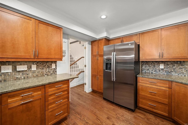 kitchen with stainless steel fridge with ice dispenser, hardwood / wood-style floors, backsplash, and light stone counters