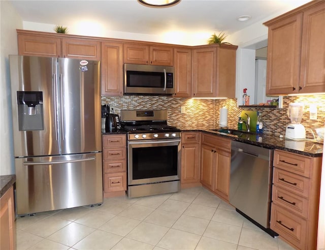 kitchen with sink, dark stone countertops, backsplash, stainless steel appliances, and light tile patterned flooring