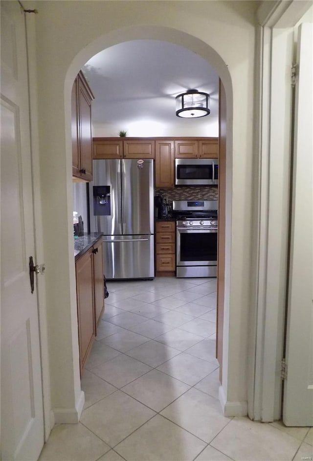 kitchen featuring tasteful backsplash, stainless steel appliances, dark stone countertops, and light tile patterned flooring